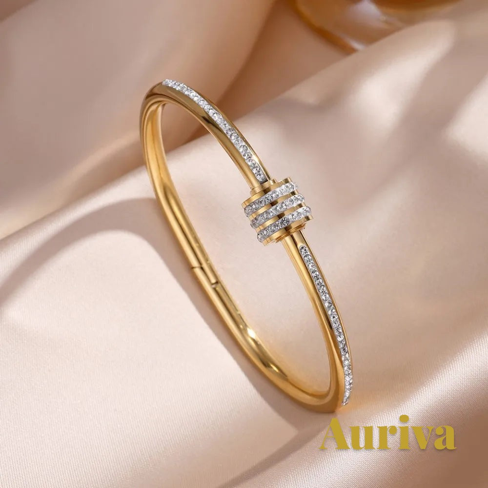 Gr8est Auriva gold titanium steel bangle featuring pave-set cubic zirconia accents on a satin fabric background.