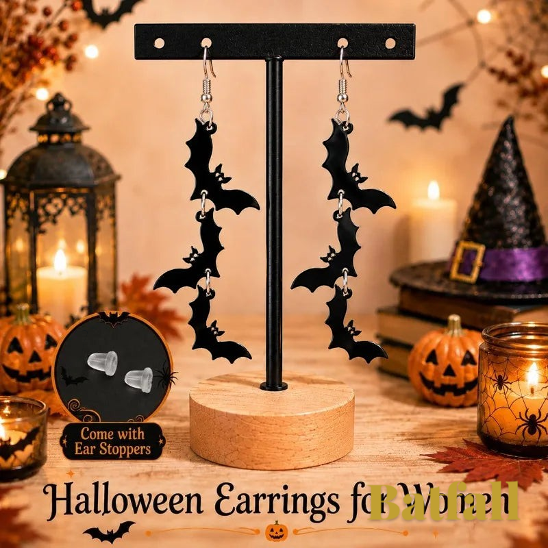 Gr8est black bat-shaped drop earrings displayed on a stand with a festive Halloween background of pumpkins and a witch hat.