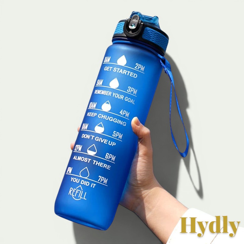 Gr8est blue 1L motivational water bottle with time markers and straw held in hand against a clear blue sky