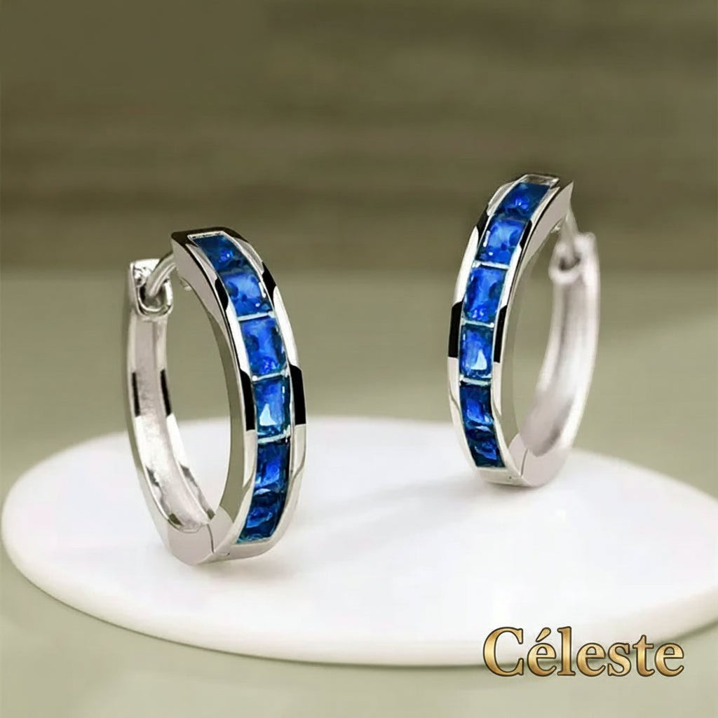 Gr8est Céleste hoop earrings featuring princess-cut blue cubic zirconia stones set in a polished silver-tone metal.