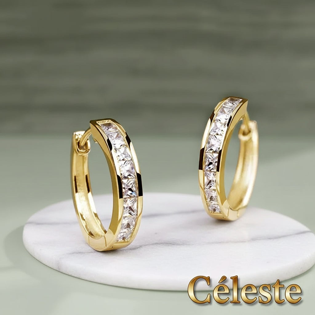 Gr8est Céleste gold-tone hoop earrings featuring princess-cut cubic zirconia stones on a marble display stand.