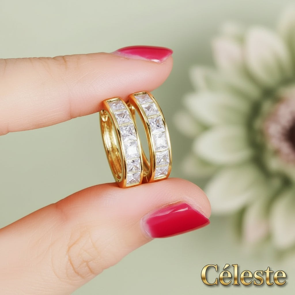 Gr8est Céleste gold-tone hoop earrings featuring princess-cut cubic zirconia stones held between fingers.