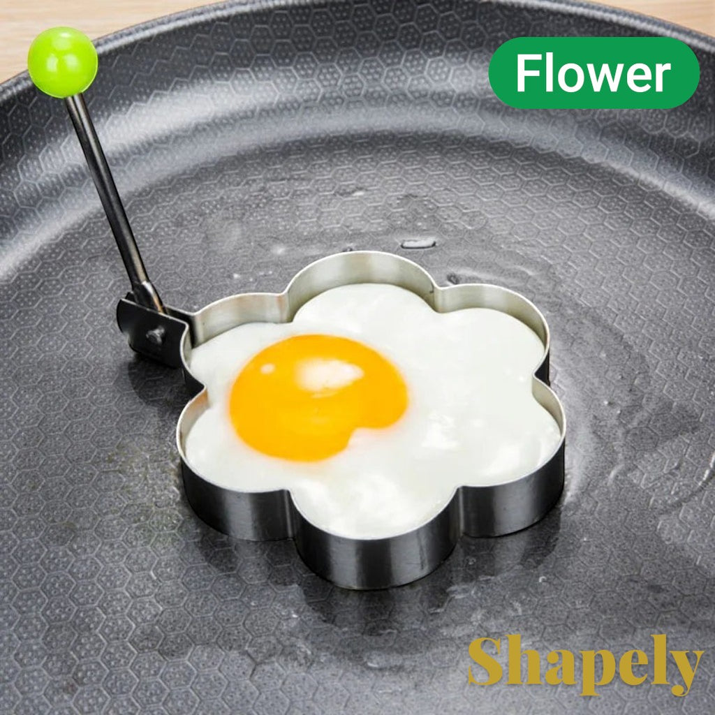 Gr8est stainless steel flower-shaped egg mold cooking a fried egg in a non-stick pan with a green handle grip