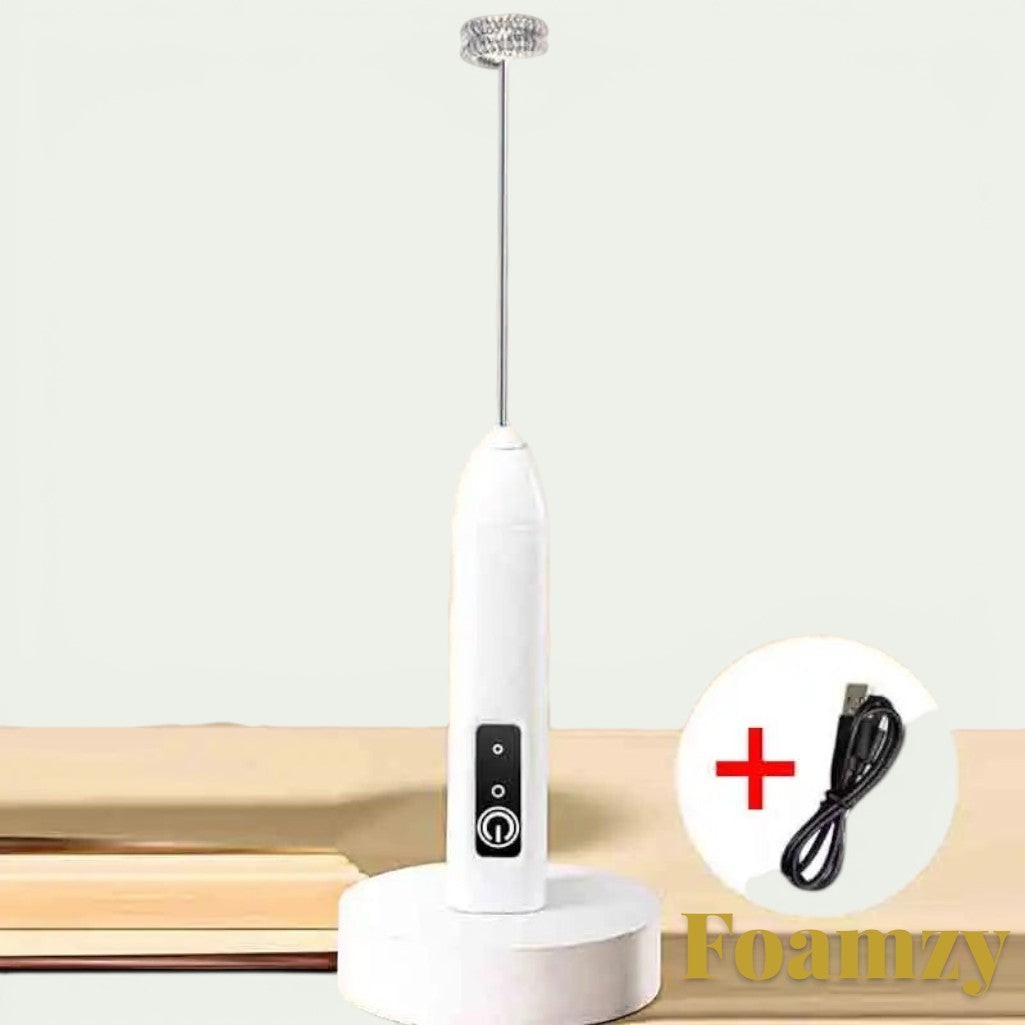 Gr8est Foamzy electric handheld milk frother and egg beater in white with a charging cable on a wooden surface.