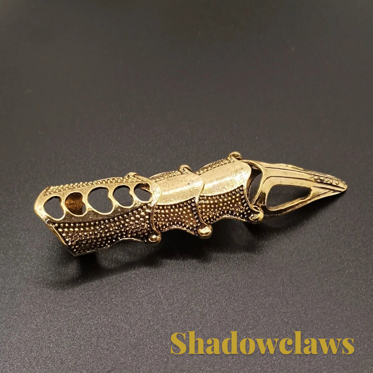 Gr8est gold-tone steampunk claw ring with articulated segments and textured metal finish on a dark background