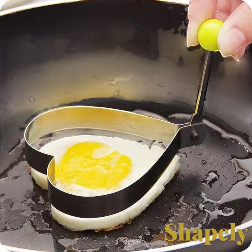 Gr8est heart-shaped stainless steel egg mold cooking ring with a yellow handle being used in a frying pan.