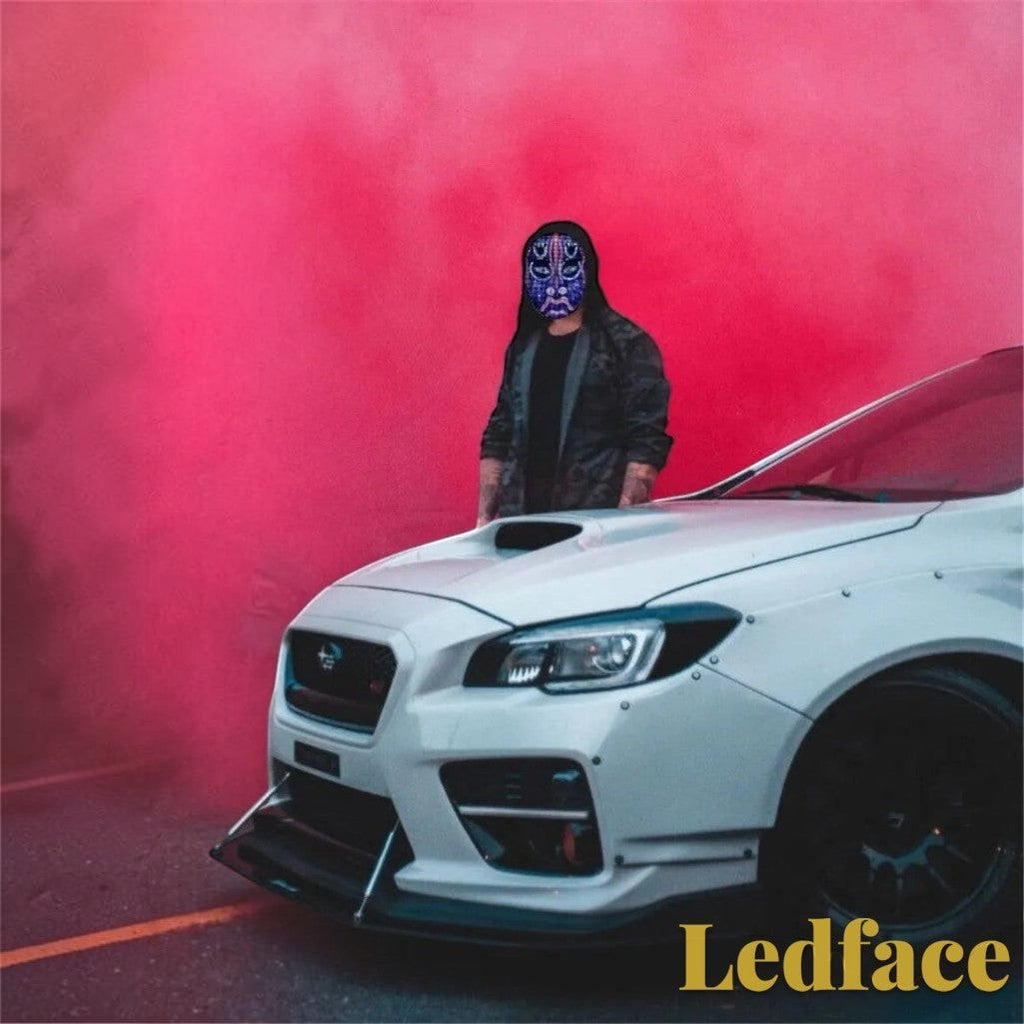 Gr8est Ledface Bluetooth RGB LED mask worn by a person in a hoodie standing by a white sports car with red smoke.