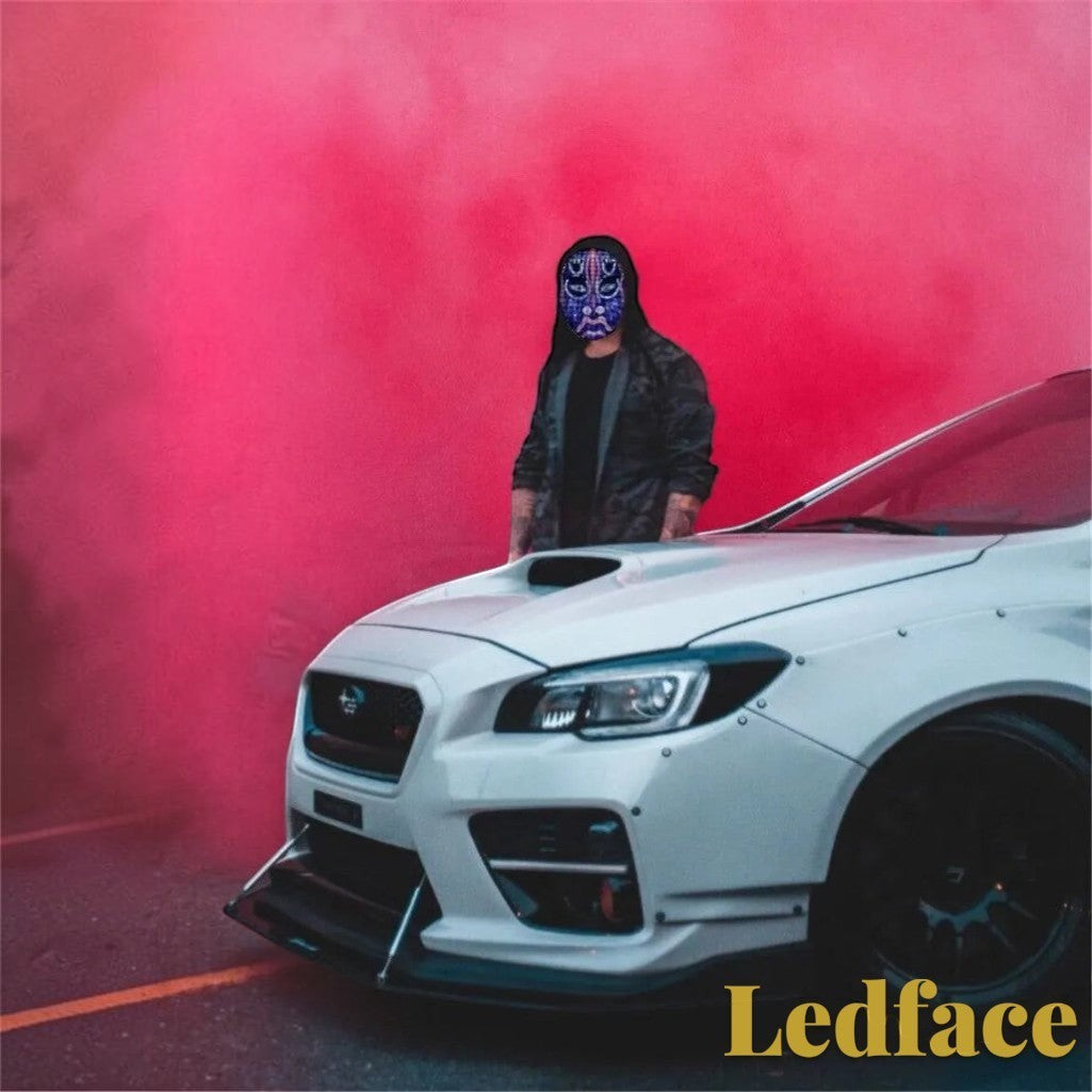Gr8est Ledface Bluetooth RGB LED mask worn by a person in a hoodie standing by a white sports car with red smoke.