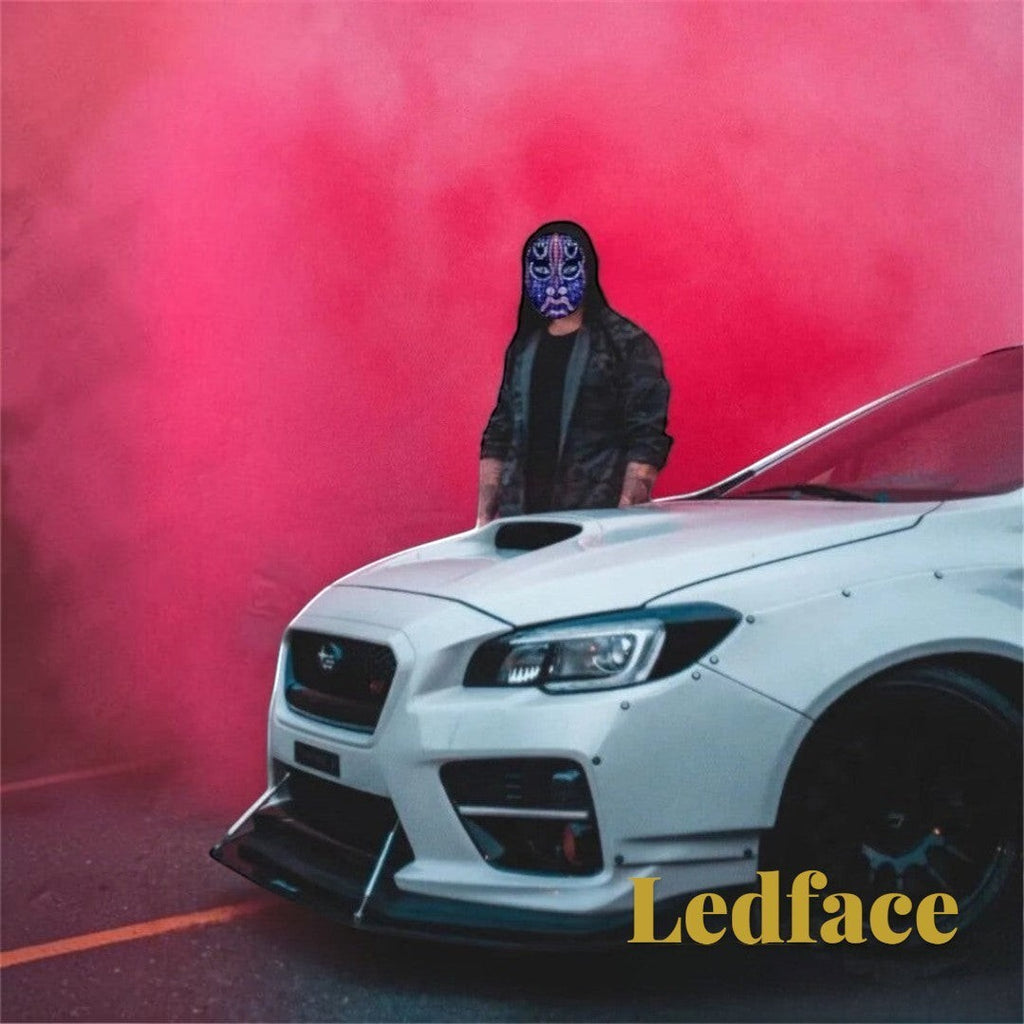Gr8est Ledface Bluetooth RGB LED mask worn by a person in a hoodie standing by a white sports car with red smoke.