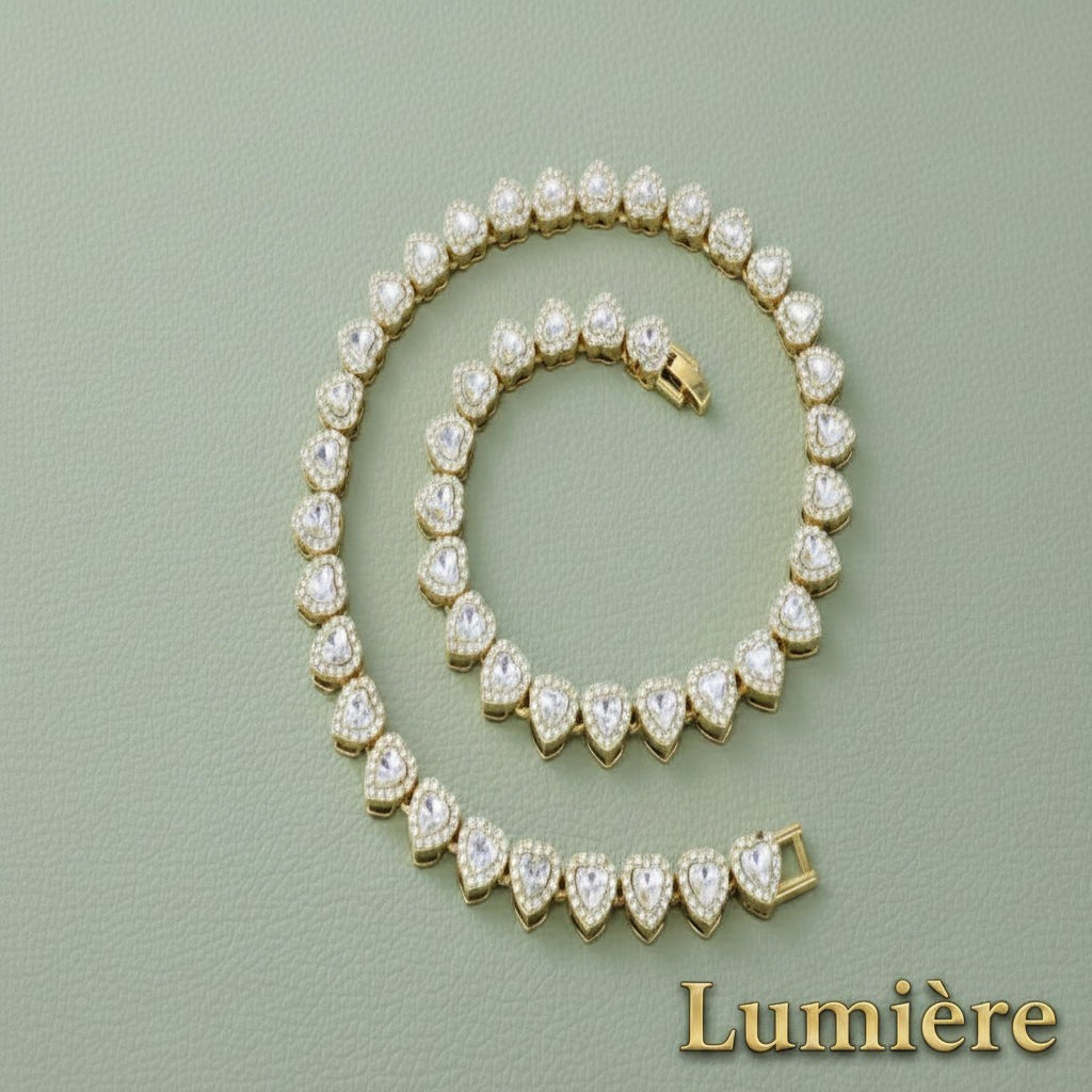 Gr8est Lumière gold heart tennis chain necklace and bracelet set with sparkling rhinestones on a green background.