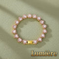 Gr8est Lumière heart tennis bracelet in gold with pink rhinestone accents on a textured green background.