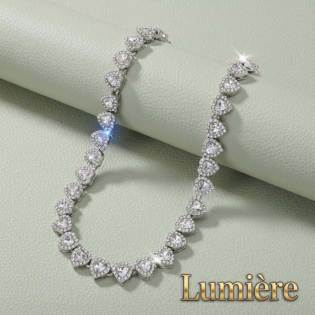 Gr8est Lumière heart tennis necklace in silver-tone zinc alloy with sparkling clear rhinestones on a green surface.