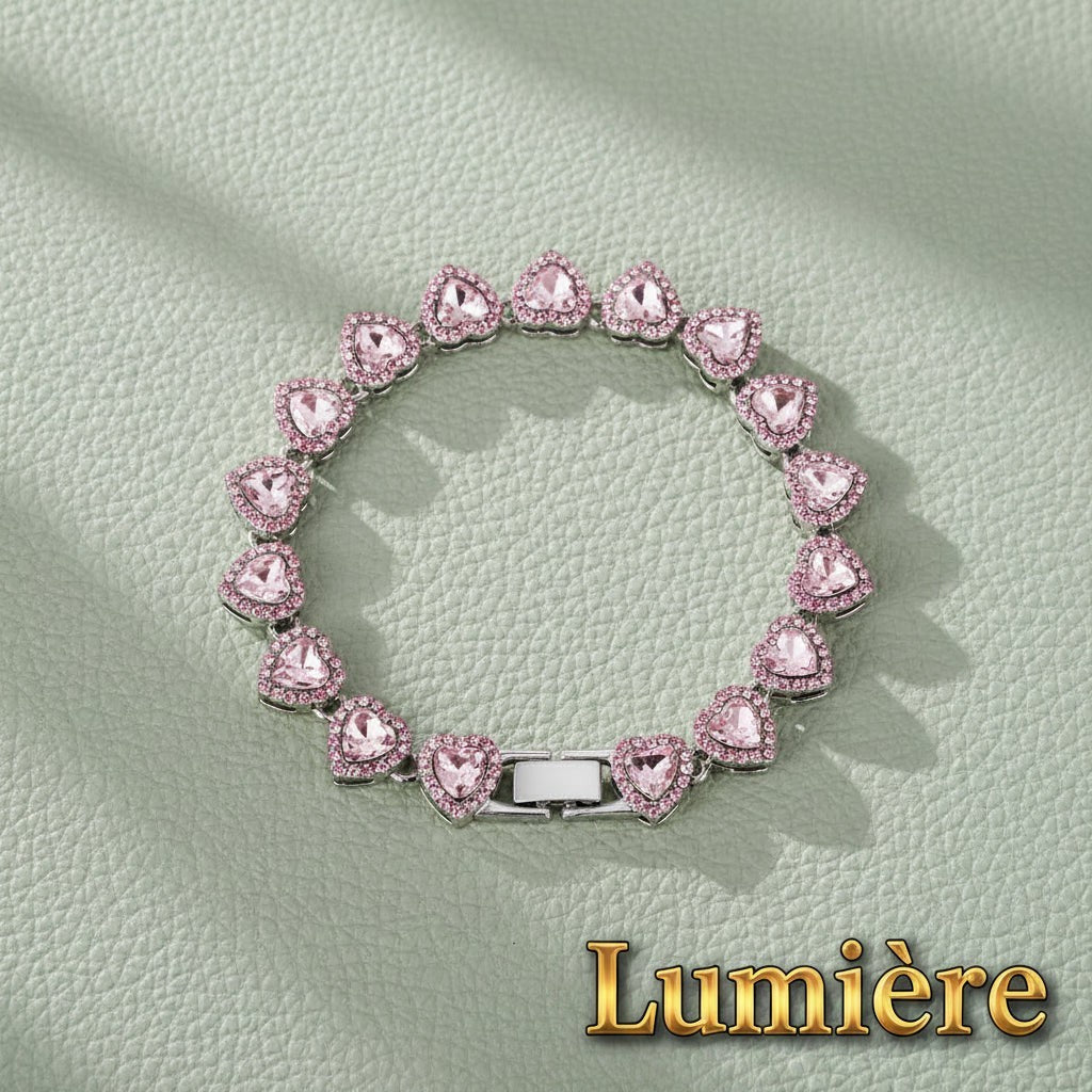Gr8est Lumière heart tennis bracelet in silvery pink with sparkling rhinestones on a textured green background.
