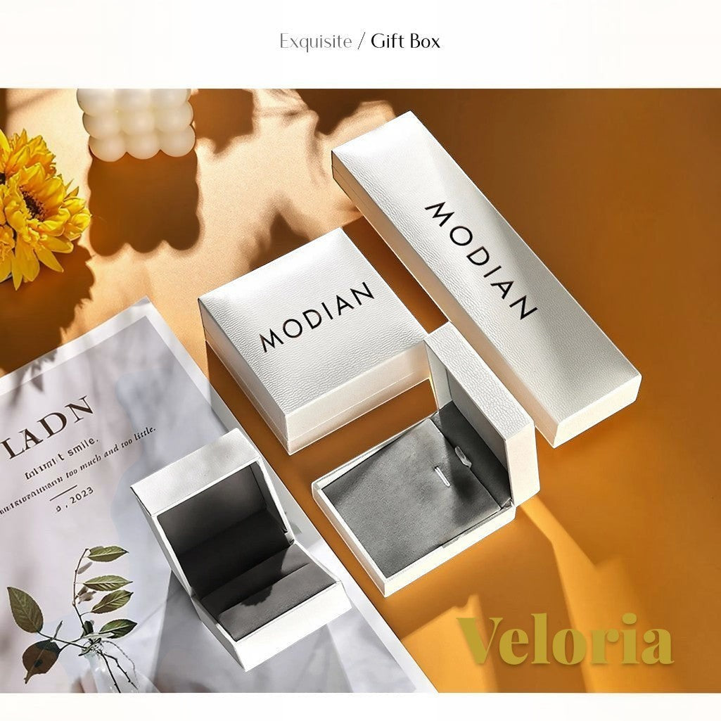 Gr8est white MODIAN branded jewelry gift boxes for the Veloria moissanite pendant necklace on a warm yellow surface.