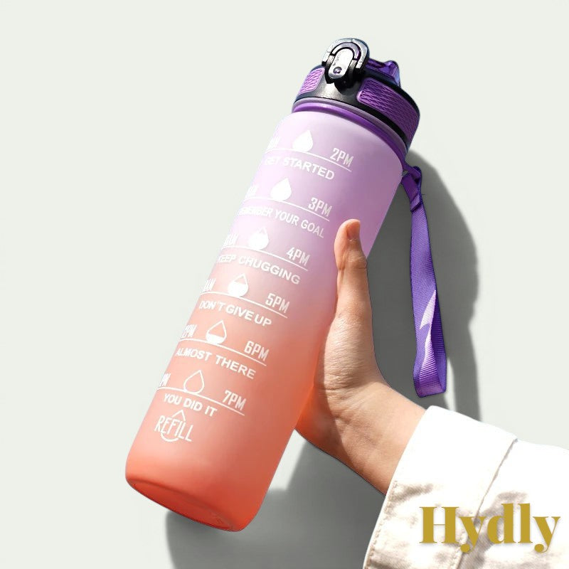 Gr8est 1L motivational water bottle in purple and orange gradient with time markers and straw held in hand.