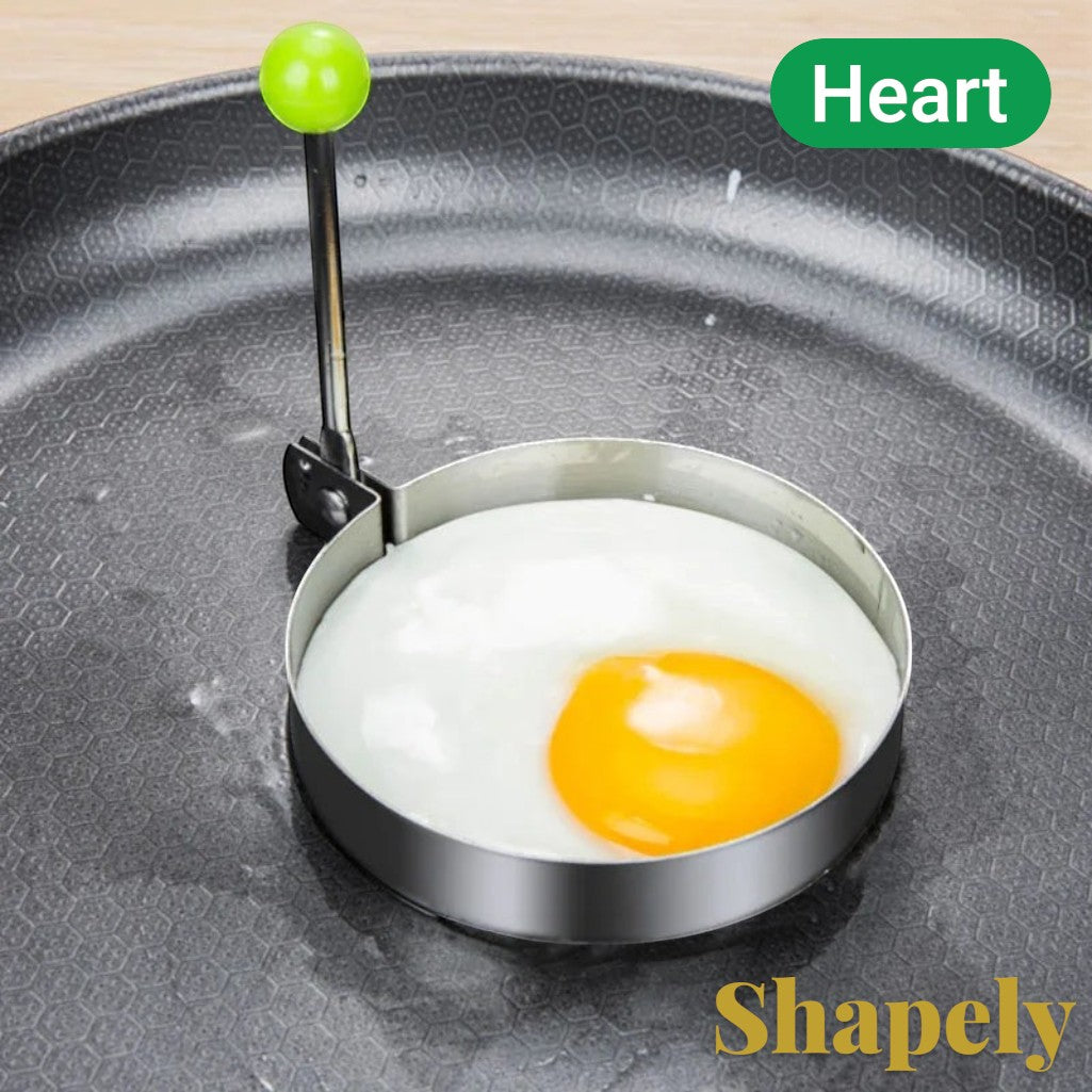 Gr8est stainless steel round egg mold with a green handle cooking a fried egg in a non-stick frying pan