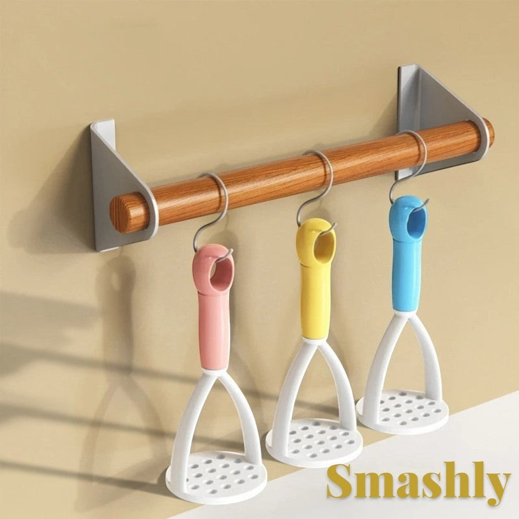 Gr8est Smashly potato mashers in pink, yellow, and blue hanging on a wooden kitchen rack
