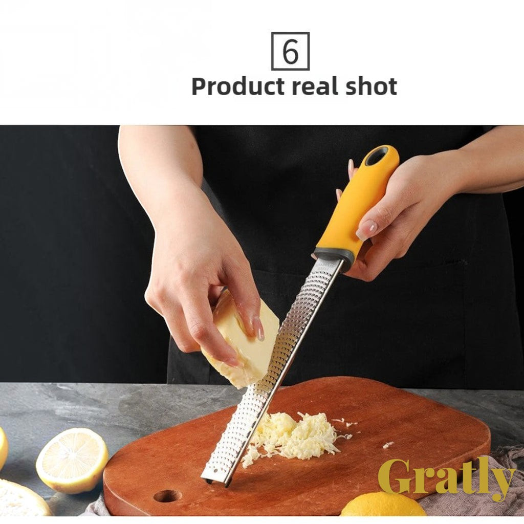 Gr8est stainless steel multi-purpose grater with a yellow ergonomic handle grating cheese on a wooden board