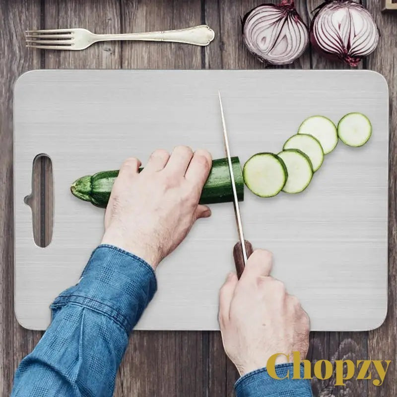 Gr8est stainless steel cutting board being used to slice zucchini on a wooden kitchen surface