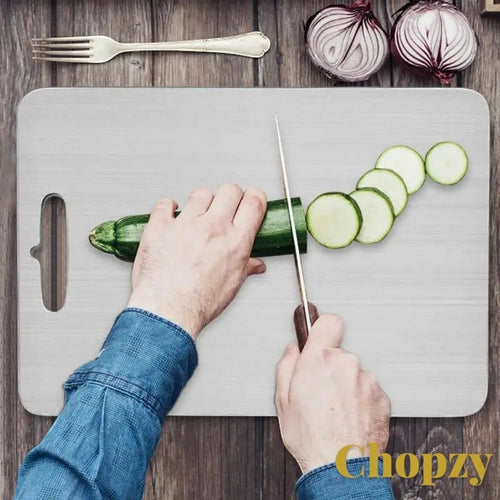 Gr8est stainless steel cutting board being used to slice zucchini on a wooden kitchen surface