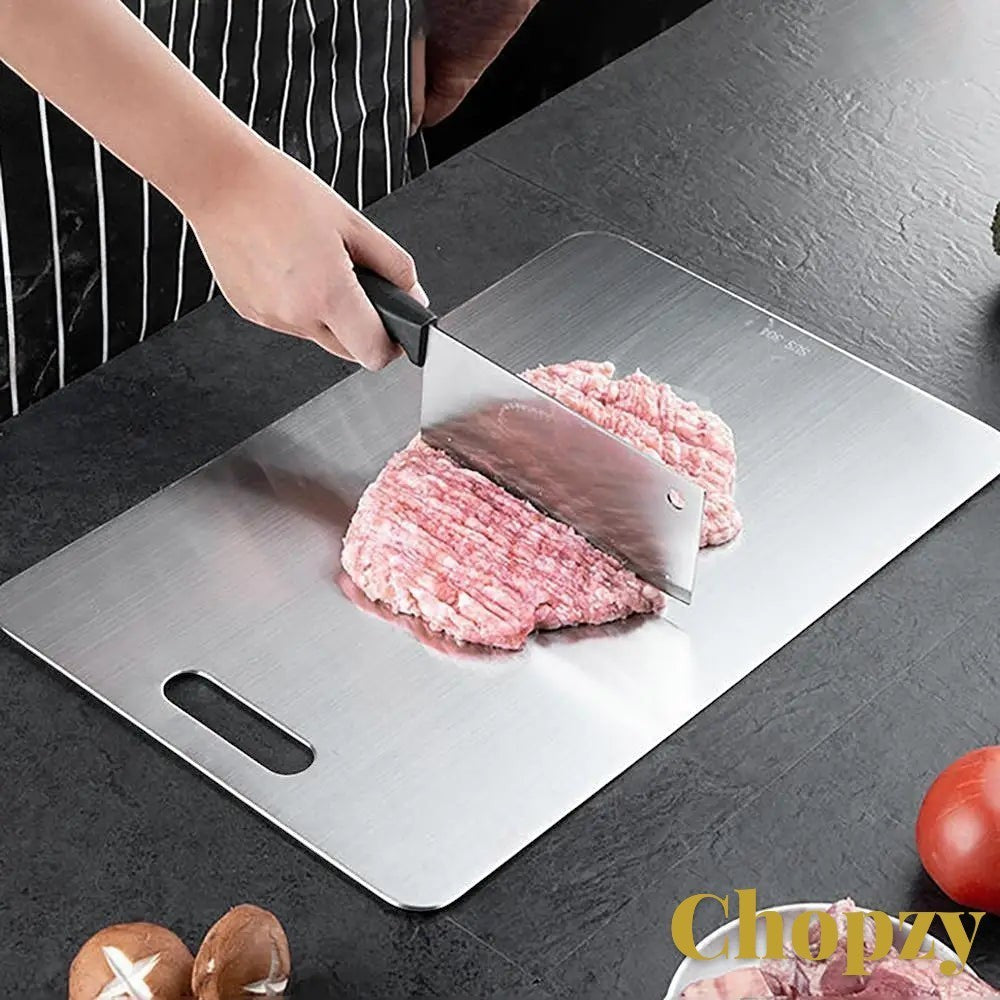 Gr8est stainless steel cutting board being used to chop meat on a dark kitchen countertop