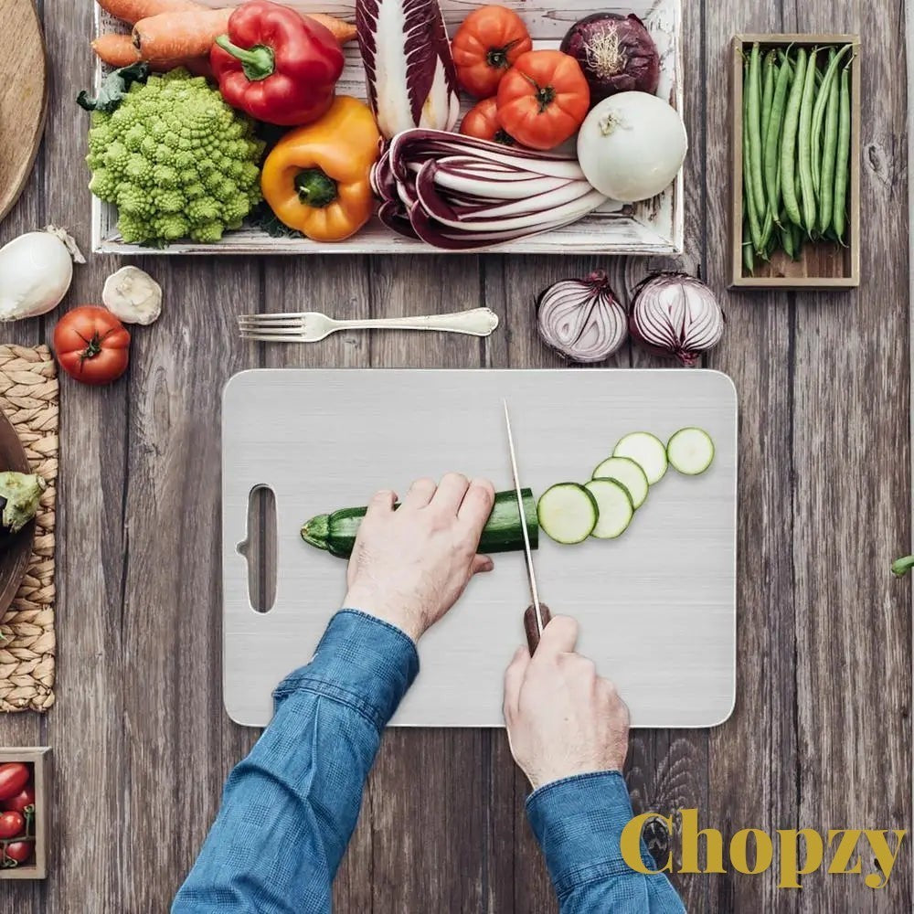 Gr8est stainless steel cutting board with hands slicing zucchini on a rustic wooden kitchen table with fresh vegetables