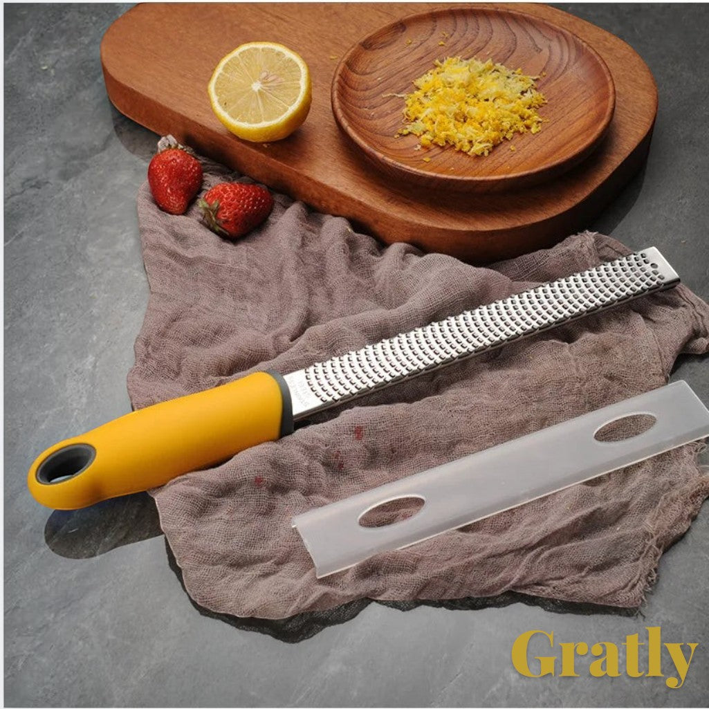 Gr8est stainless steel multi-purpose grater with a yellow ergonomic handle, shown with a protective cover and lemon zest.