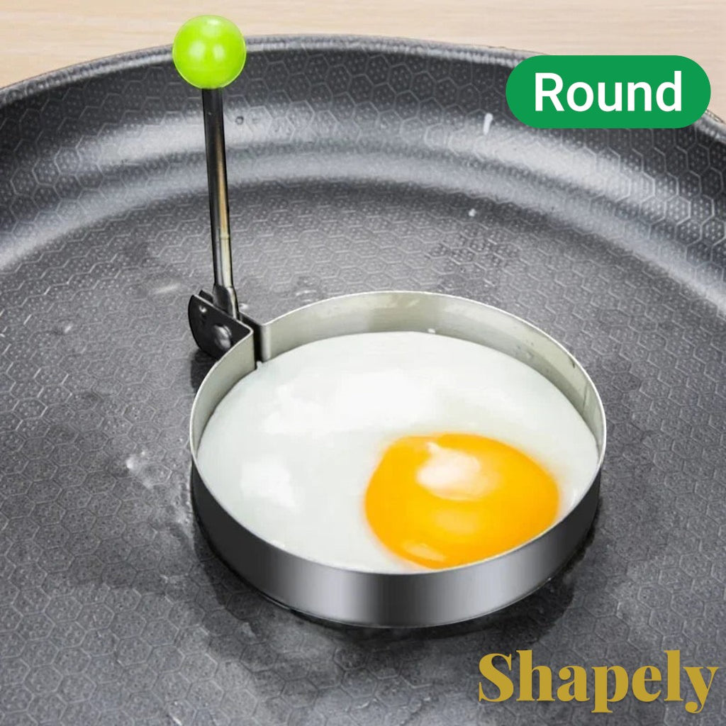 Gr8est stainless steel round egg mold cooking ring with green handle on a non-stick frying pan