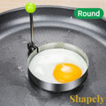 Gr8est stainless steel round egg mold cooking ring with green handle on a non-stick frying pan