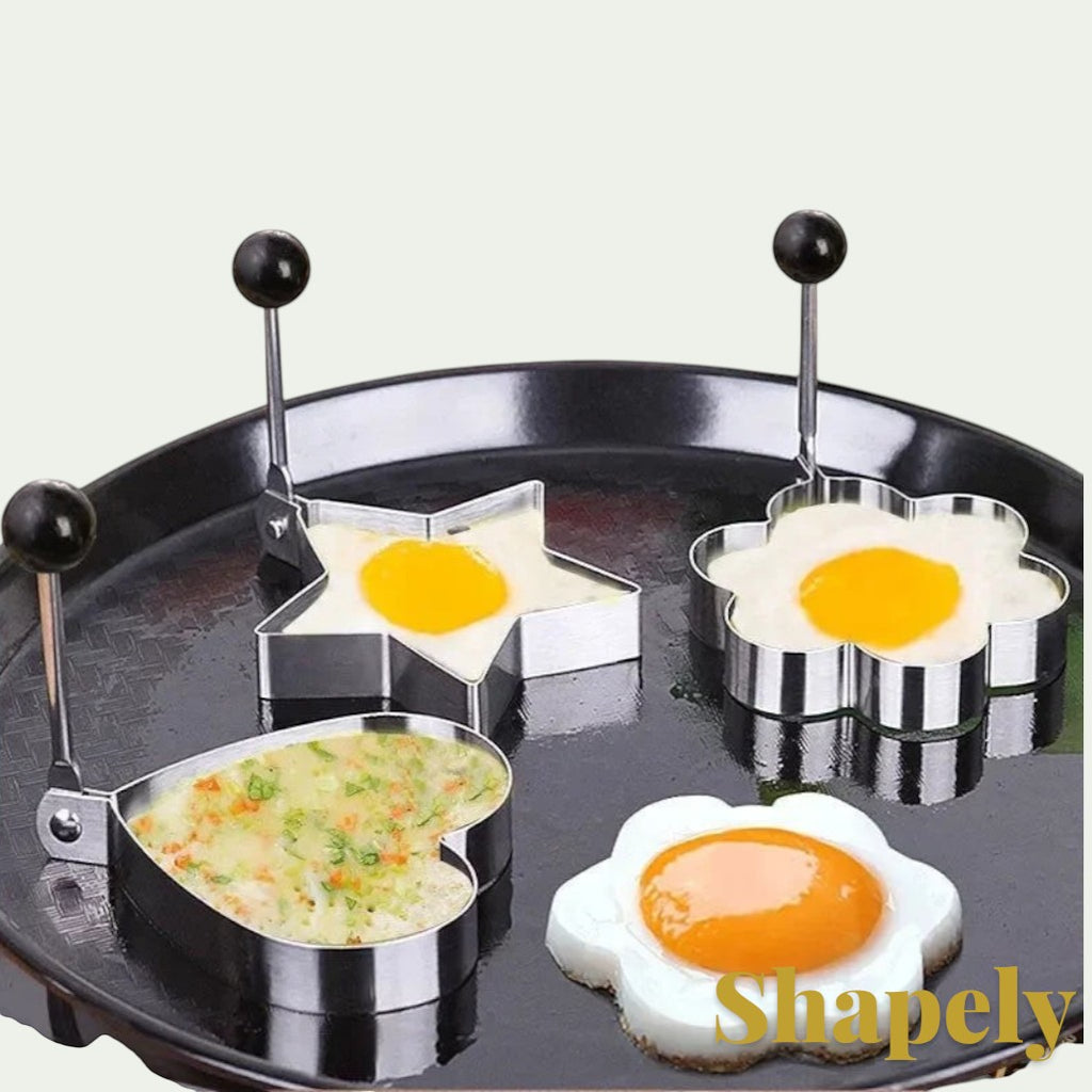 Gr8est stainless steel egg and pancake molds in heart, star, and flower shapes cooking on a black frying pan.