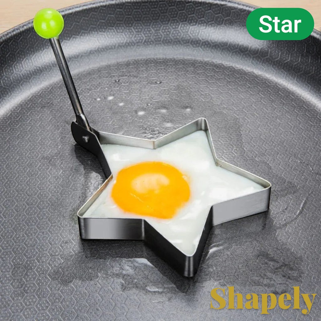 Gr8est star-shaped stainless steel egg and pancake mold with a green handle on a non-stick frying pan