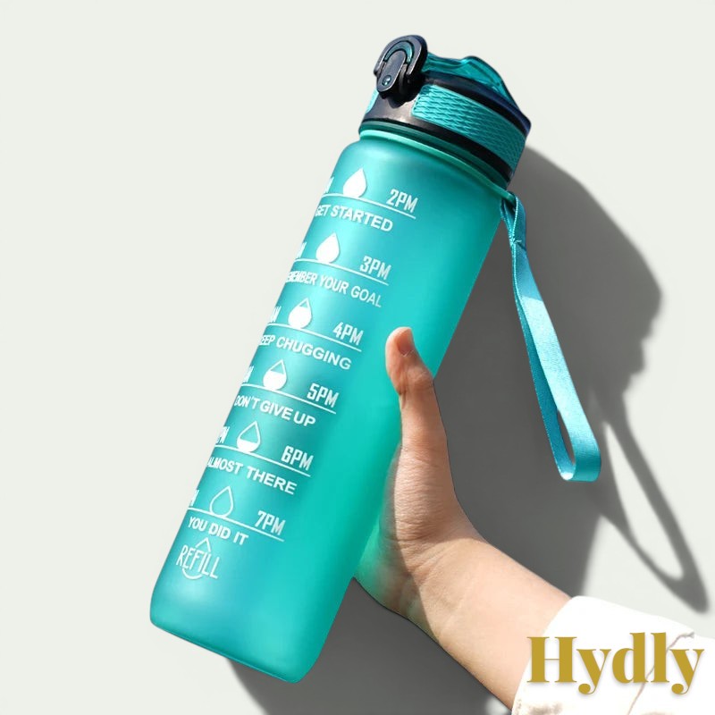 Gr8est 1L teal motivational water bottle with time markers, straw, and leak-proof lid held against a blue sky.