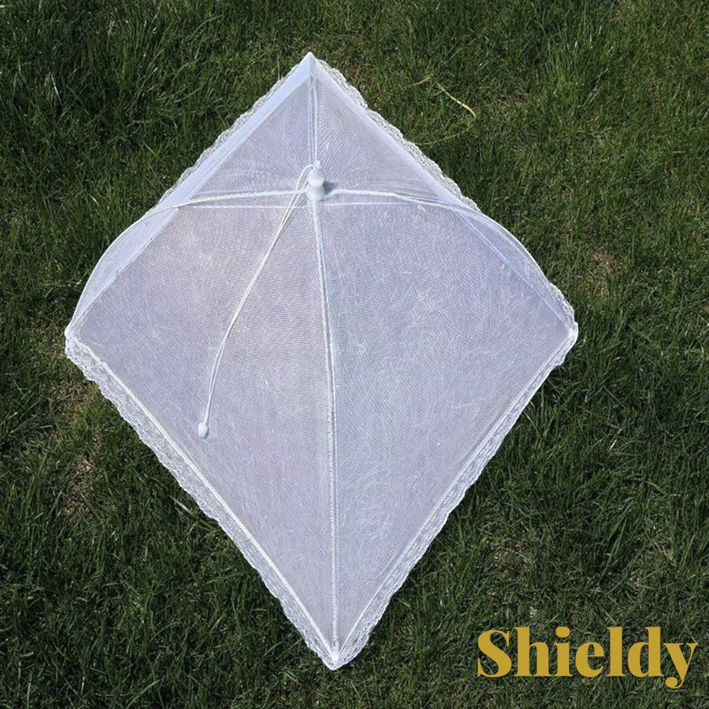 Gr8est white pop-up mesh food cover with lace trim, protecting food from insects on outdoor grass.