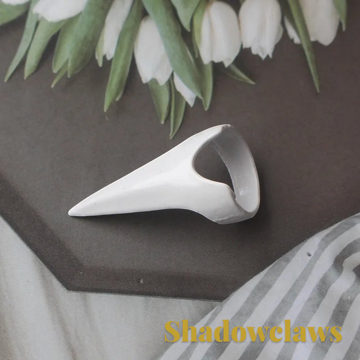 Gr8est white steampunk claw ring with a smooth finish, resting on a dark surface near white tulips.